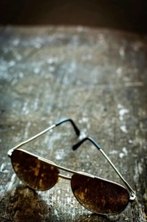 Sleek sunglasses rest on a weathered wooden surface, reflecting softly diffused light. The