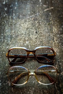 A collection of vintage eyeglasses rests on a rustic wooden surface, illuminated by warm lighting
