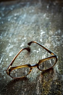 A pair of vintage glasses lies on a weathered wooden table. The unique design is illuminated by