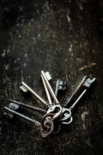 A collection of vintage keys is arranged on a rustic wooden surface. The dark background emphasizes