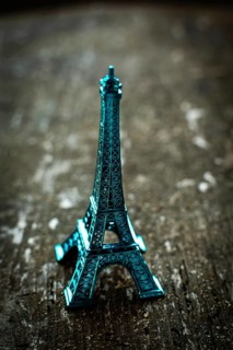 A striking teal miniature Eiffel Tower stands on a rustic wooden surface, bathed in soft lighting