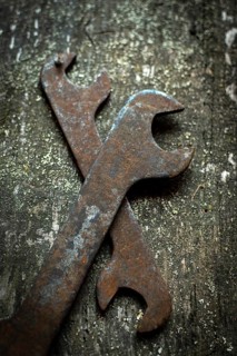 Two old wrenches rest crossed on a weathered wood surface, revealing their rust and signs of many