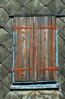 Closed wooden shutters with peeling paint rest against an aged building, highlighting the rustic