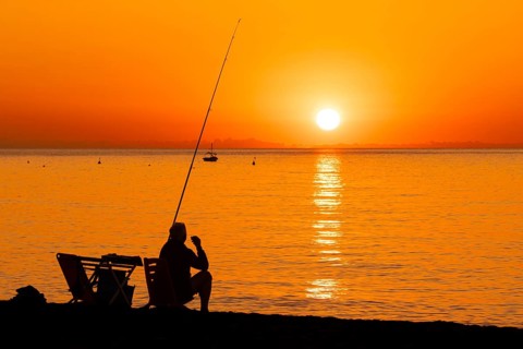 A man fishing shortly after sunrise on the Costa Rei, a stretch of coastline on the Italian island