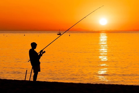 A boy fishing shortly after sunrise on the Costa Rei, a coastline of the Italian island of