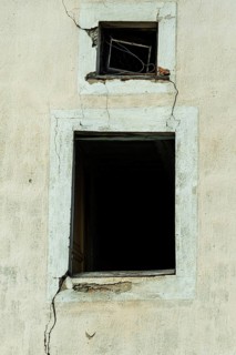 Cracked walls and dark empty windows show the neglect of an abandoned structure. The peeling paint