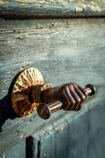 A distinctive door handle resembling a hand grips a rustic wooden door, featuring intricate details