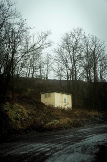 A small yellow building stands alone atop a dark hill, surrounded by bare trees. The atmosphere is