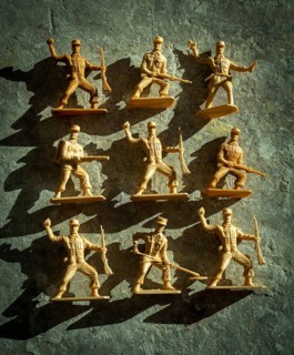 Plastic toy soldiers are displayed in different action poses on a textured surface, casting shadows