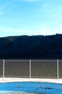 A swimming pool reflects the blue sky and surrounding mountains. A metal fence surrounds the space,