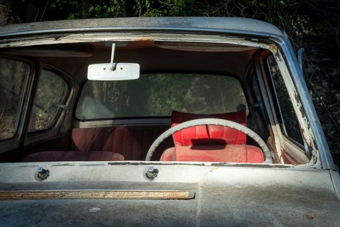 A deserted vintage car sits in a state of disrepair, showcasing a cracked windshield and a faded