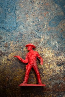 A red cowboy figure is positioned confidently with a raised finger, set against an intriguing
