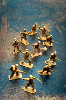 Small toy soldiers are positioned in a playful arrangement on a rough surface. Their poses suggest