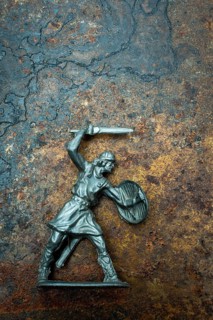 A detailed warrior figure stands ready for battle, gripping a sword in one hand and a shield in the