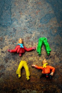 Four vibrant plastic figures with missing heads and different clothing pieces are creatively