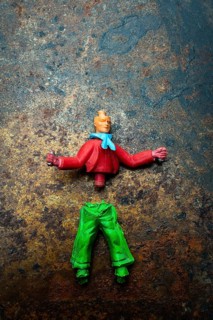 Brightly colored toy figure parts lie scattered on a rusted metal surface, showcasing a mix of red