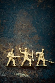Three vintage toy soldiers in different poses rest on a rugged, textured surface. Their playful
