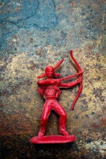 A red plastic toy archer represents a Native American figure, posed with a bow and arrow on a