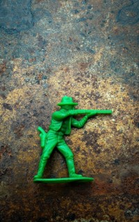 A small green plastic toy cowboy stands firmly on a rustic blue and brown textured background. The