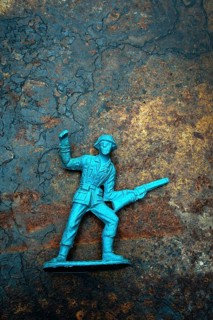 A vintage toy plastic soldier stands defiantly with a raised fist and a gun, symbolizing courage