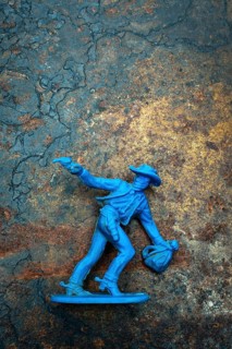A bright blue cowboy figure stands firmly on a rugged surface, one hand raised with a pistol while