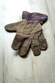 A leather glove, showing signs of age and wear, is placed flat on a textured wooden surface. The