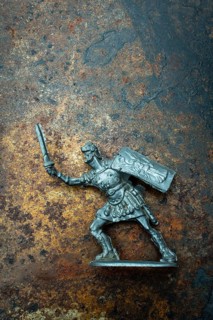 A roman soldier figure stands ready for combat, holding a sword in one hand and a shield in the