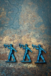 Three small blue toy soldiers are positioned on a rough, textured surface, representing scenes from