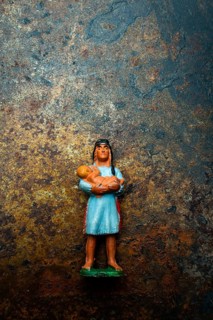 A vibrant plastic figure represents an Indian Native American woman cradling a child, positioned on