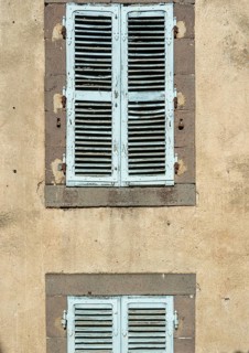 Two sets of vintage blue shutters add charm to a weathered wall, showcasing the beauty of rustic