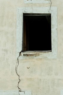 A cracked wall features an empty window opening, creating a stark contrast against the faded