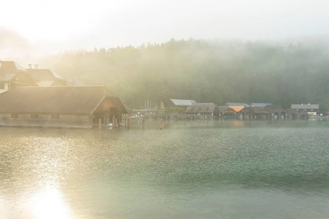Mystical morning at Königssee in Schönau with boathouses. Sunrise and beautiful wafts of mist over