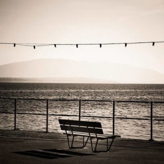 A solitary bench sits by the lakeside promenade in Nyon, Switzerland. Gentle waves ripple in Geneva