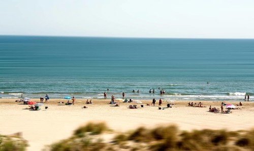 Sunbathers and swimmers relax on the sandy beach by the tranquil Mediterranean Sea. The atmosphere