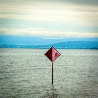 A prominent red information sign rises above the water of Lake Geneva, indicating safety or