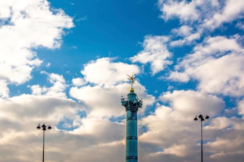 The July Column rises majestically in the Place de la Bastille, surrounded by fluffy clouds. This