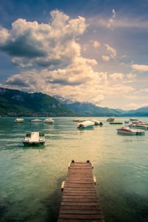 A wooden pontoon extends over the tranquil waters of Annecy Lake, surrounded by mountains and