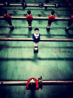 A lively table football game features diverse player figures in red, blue, and black, positioned on