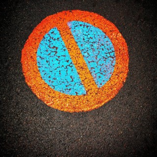 A vibrant no parking symbol is prominently displayed on a black asphalt surface, featuring a blue