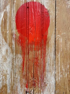 A vivid red circular splash vividly contrasts against a rustic wooden background. The paint appears