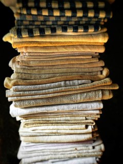 A neat stack of folded textiles in various shades of beige, cream, and a hint of black is