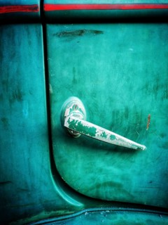 A close-up view of a vintage car door handle featuring a weathered surface and vibrant green paint.