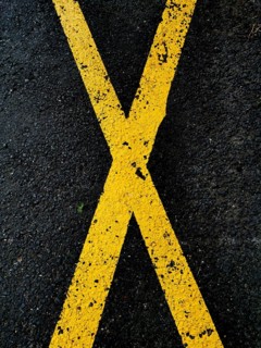 A pattern of yellow crossing lines painted on a dark asphalt surface emphasizes a bold visual