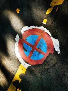 A circular parking symbol with red and blue colors appears worn and cracked on an asphalt surface.
