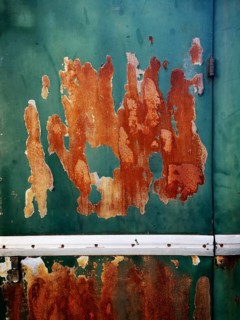 A weathered green metal surface displays extensive rust patches and peeling paint, highlighting the