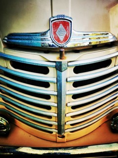 The front grille of a vintage truck features intricate chrome detailing with a prominent emblem.