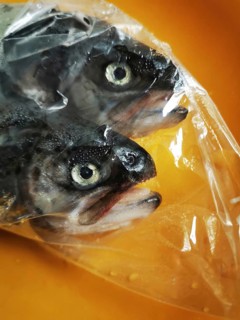 Two whole fish with dark skin and distinct eyes are packaged in transparent plastic, lying on an