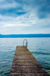A sturdy jetty extends into the serene waters of Lake Geneva, surrounded by mesmerizing blue hues