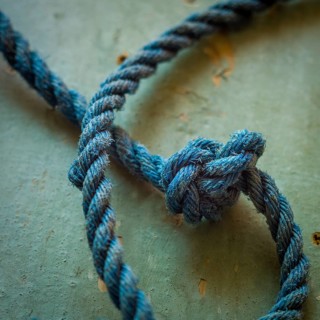 A close-up view reveals an intricately tied blue rope knot resting on a textured surface,