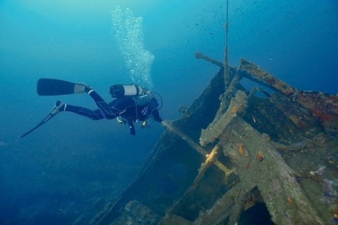 Diver floats near a shipwreck while air bubbles rise to the surface. Dive site wreck Michel C,